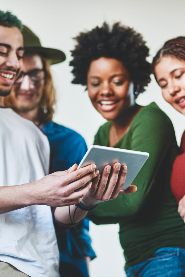 smiling mixed race men and women, all looking at a tablet.